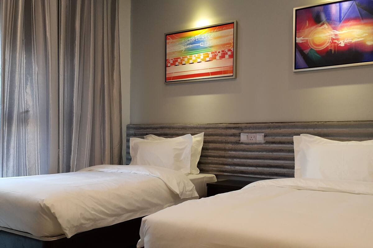 A hotel room with two beds, a headboard, a painting, and a window with curtains.