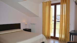 Un dormitorio con cama, mesita de noche, lámpara, ventana con cortinas y vistas al exterior.