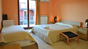 Habitación de hotel con dos camas, una mesita, una mesita de noche con lámpara y vistas a un balcón.