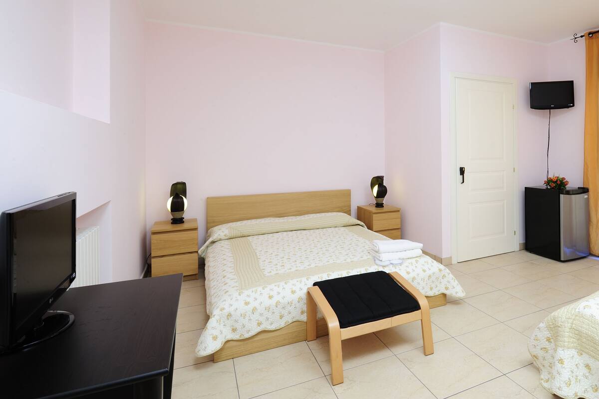 A bedroom with a bed, bedside tables, a TV, a desk, and a TV stand.