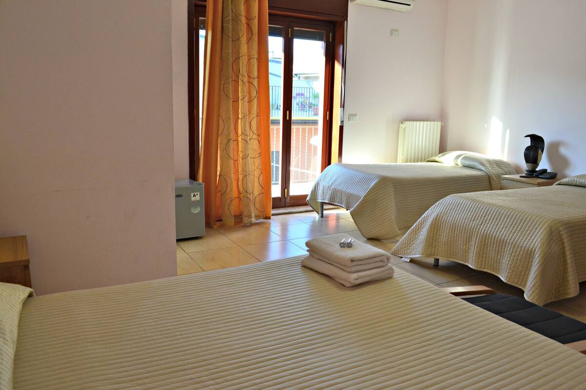 A hotel room with two beds, a radiator, a lamp, and a view of the outside.