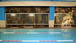 Una piscina interior con separadores de carril, un trampolín y una pared con textura rocosa.