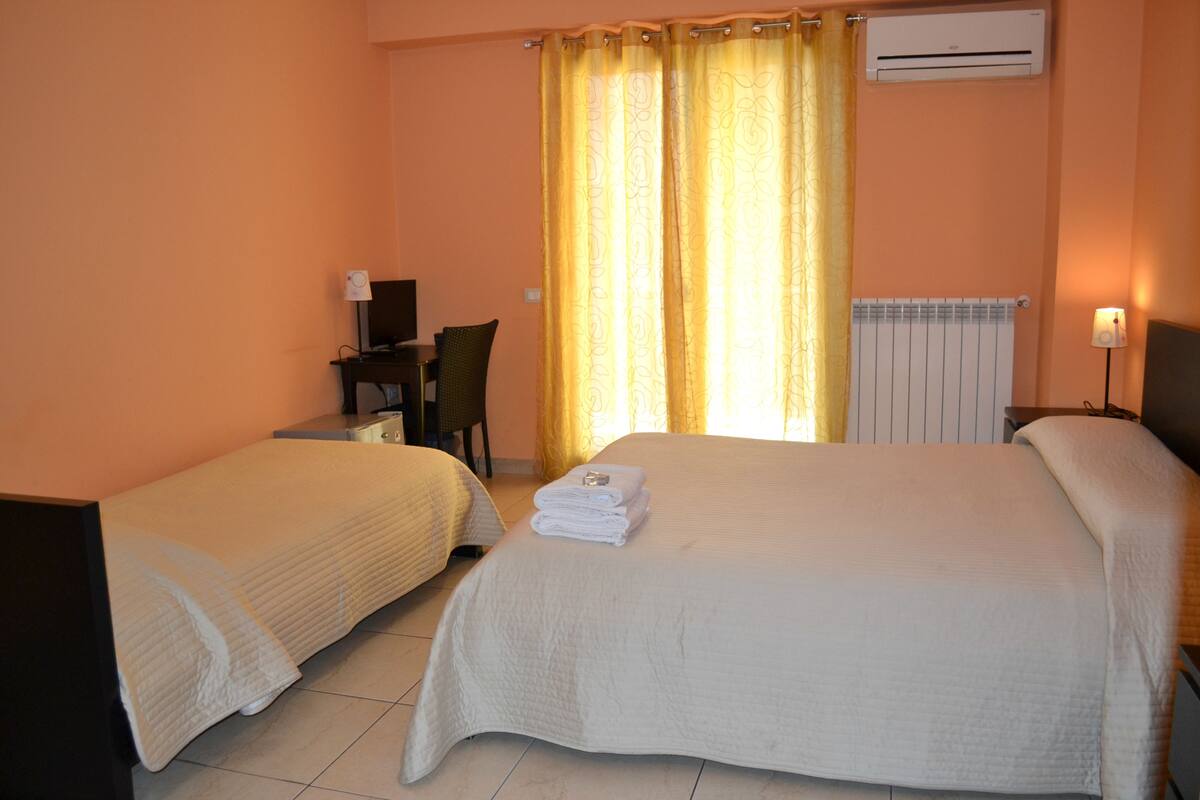 A hotel room with two beds, a desk with a chair, a lamp, and an air conditioning unit.