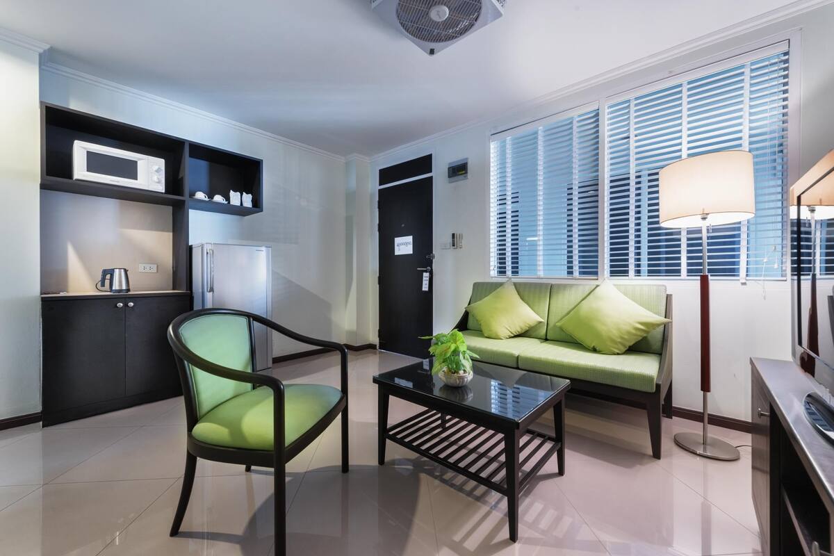 A modern living room with a sofa, a chair, a coffee table, and a kitchen area with a microwave and refrigerator.