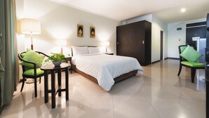 A hotel room with a bed, two chairs, a small table with a plant, and a wardrobe. - Capital Mansion (Bangkok)