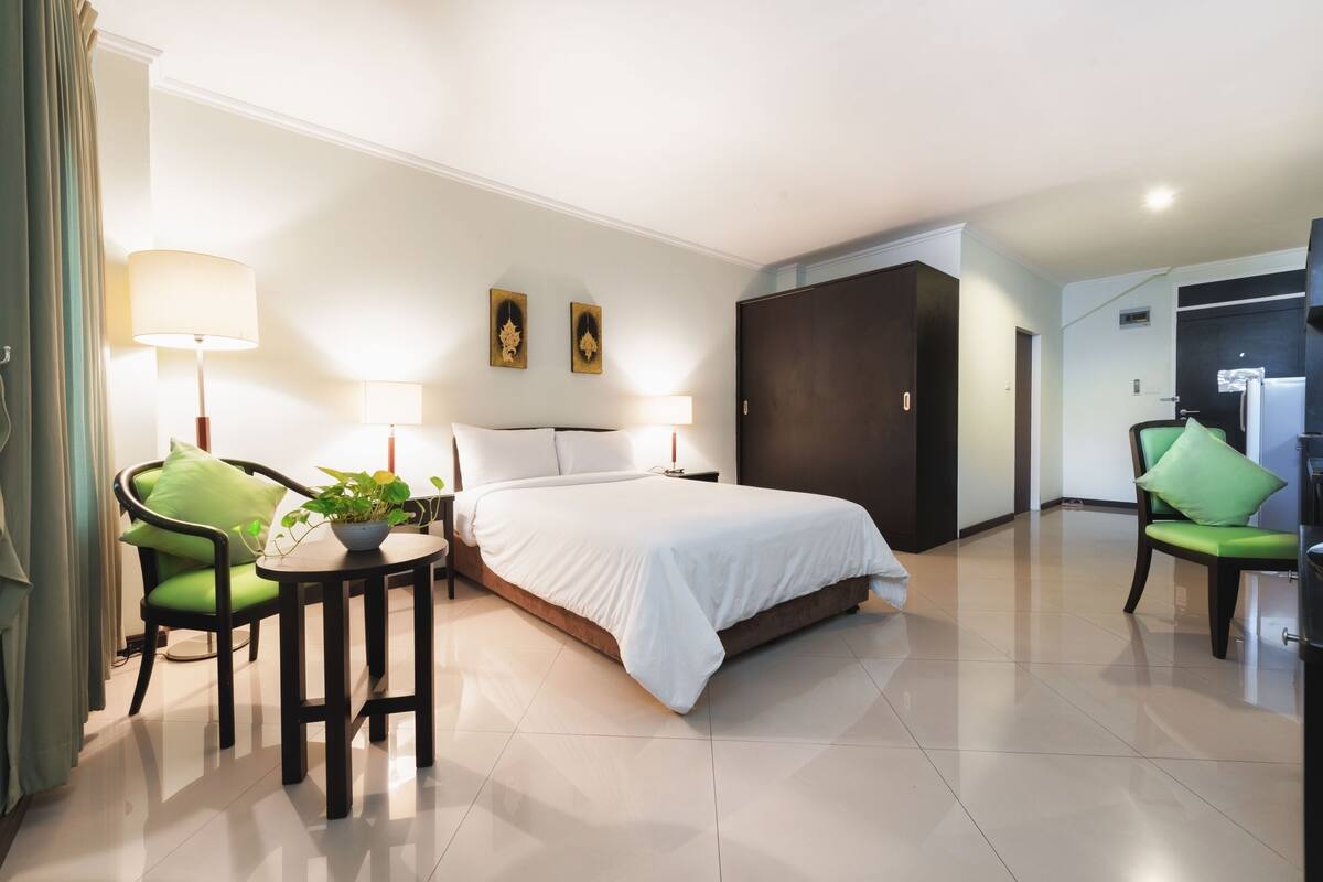 A hotel room with a bed, two chairs, a small table with a plant, and a wardrobe.