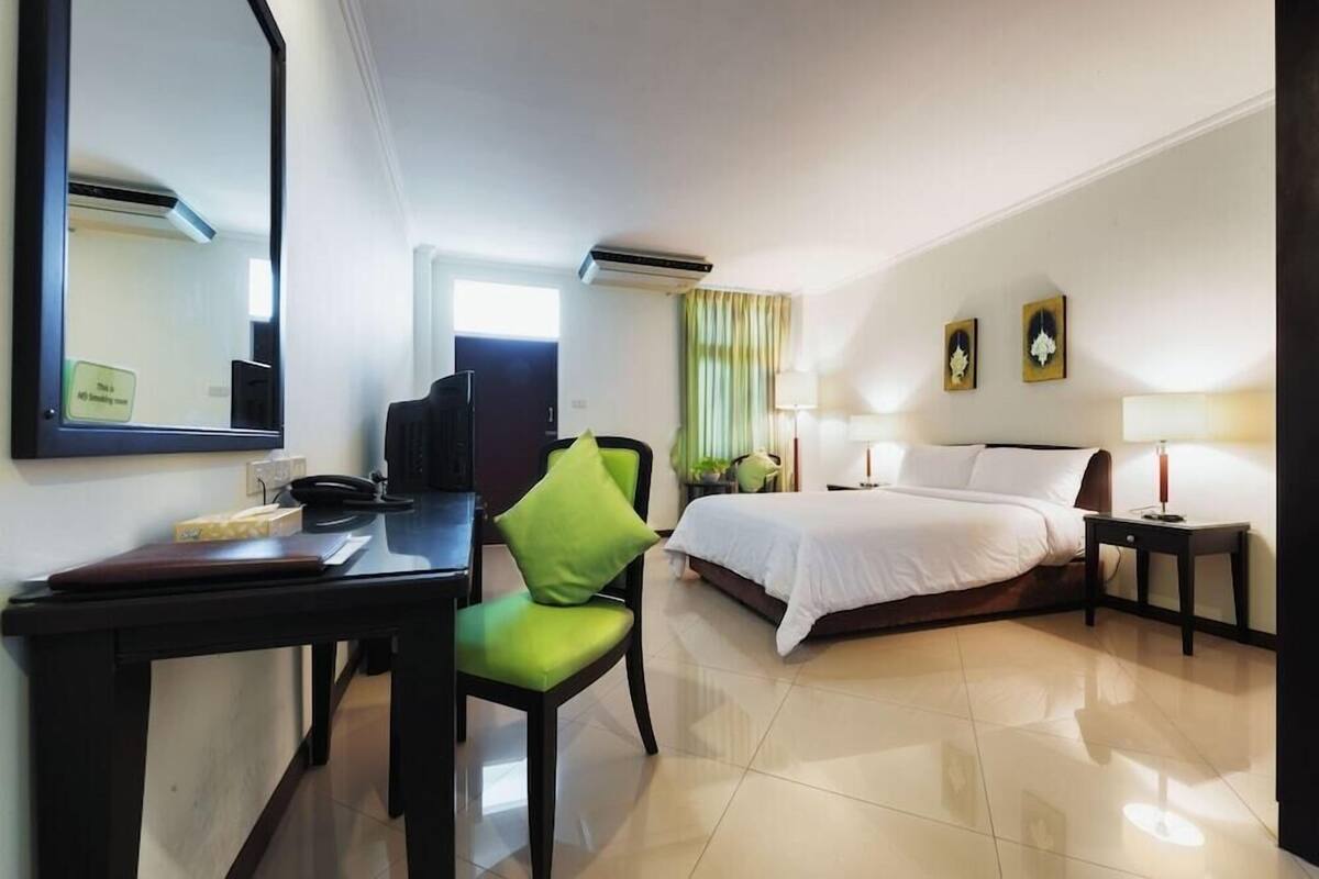 A hotel room with a bed, a desk with a telephone, a chair, a bedside table, and a mirror.