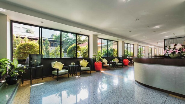 A spacious lobby with large windows, seating areas, and a reception desk. - Capital Mansion (Bangkok)
