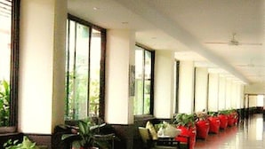 A long corridor with rows of seating and potted plants, large windows, and a polished floor. - Capital Mansion (Bangkok)