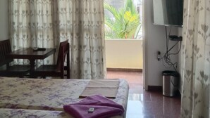 A hotel room with a bed, a table, chairs, a TV, and an air conditioning unit. - Orion Sky Wings (Kochi)