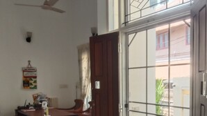 A room with a wooden desk, chairs, a ceiling fan, and a large sliding glass door leading to a garden. - Orion Sky Wings (Kochi)