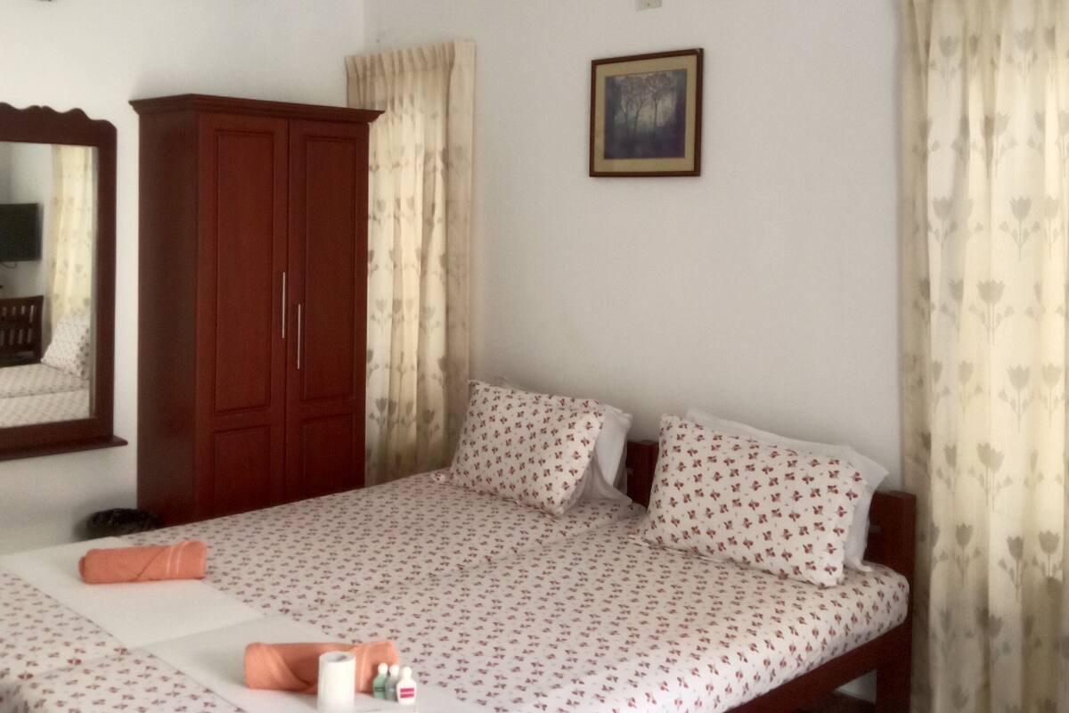 Quarto com uma cama de solteiro, guarda-roupa, ventoinha de teto, ar condicionado, quadro emoldurado e cortinas.
