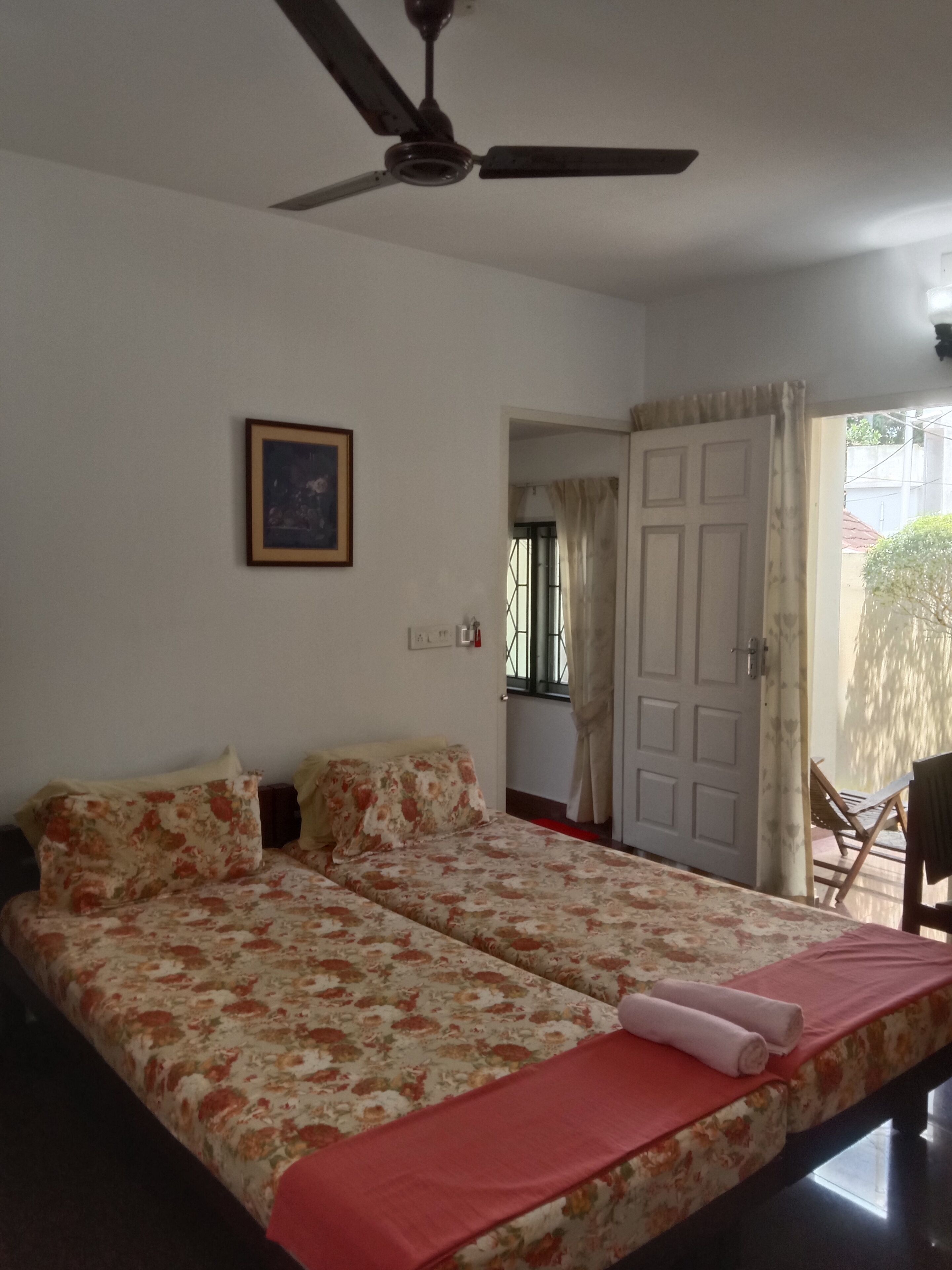 A bedroom with a bed, a ceiling fan, a framed picture on the wall, and a door leading to another room.