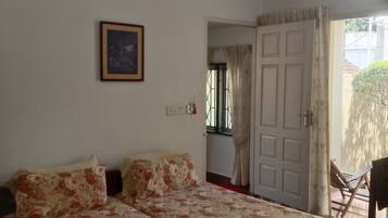 A bedroom with a bed, a ceiling fan, a framed picture on the wall, and a door leading to another room.