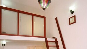 A room with a wooden staircase, a chandelier, and a seating area with chairs and a table. - Orion Sky Wings (Kochi)