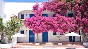 A white building with blue doors and windows, surrounded by pink bougainvillea. - Boutique Hotel Tilos Mare (Tilos)