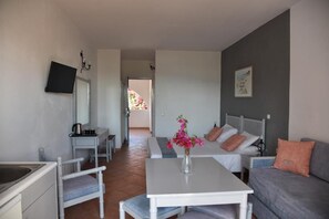 A compact hotel room with a bed, a sofa, a small table, a desk, and a TV mounted on the wall.