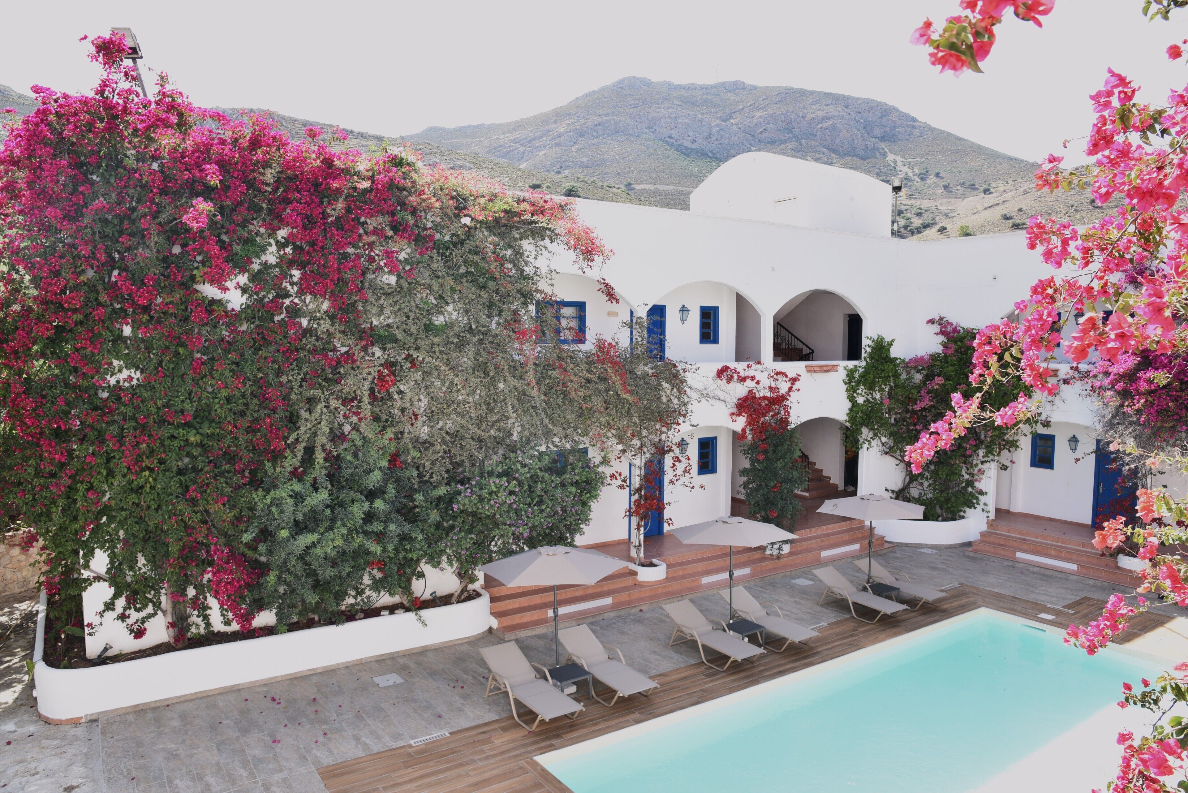 Un espace aménagé au bord de la piscine, avec des chaises longues, une piscine et un bâtiment orné d’arches et de fleurs roses.