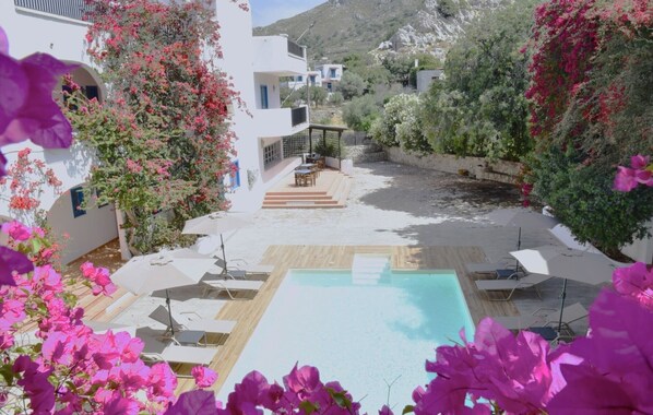 A pool area with a wooden deck, lounge chairs, and a small outdoor seating area.
