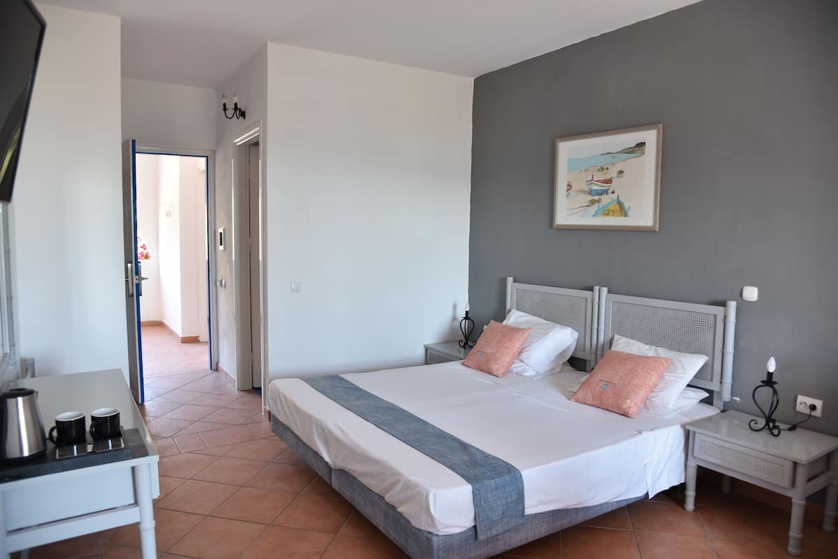 Une chambre à coucher comprenant un lit, des tables de chevet, une commode, un tableau accroché au mur et une porte donnant sur une autre pièce.