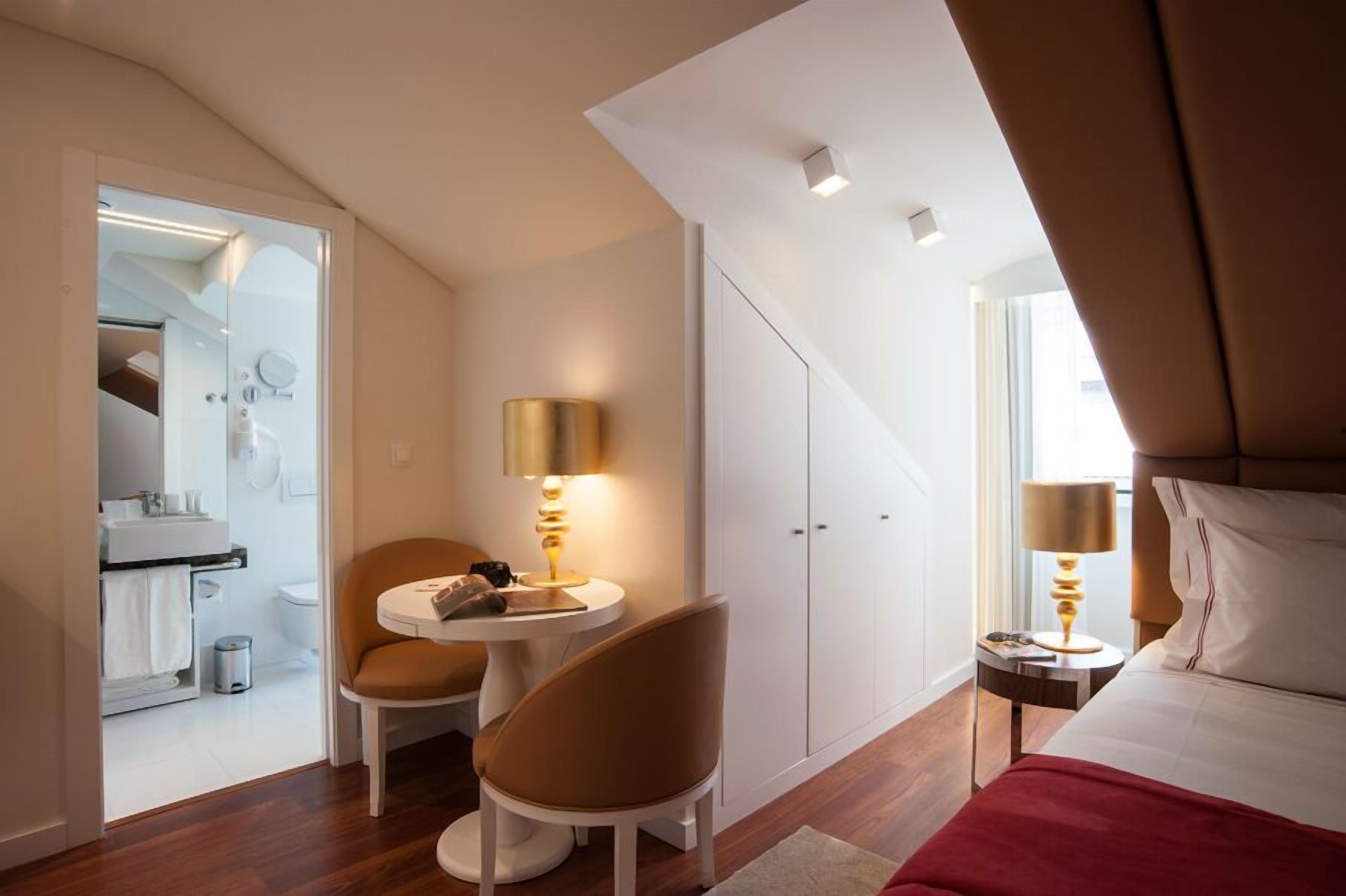 Una habitación de hotel moderna con una cama, un escritorio con lámpara, una silla y un armario.