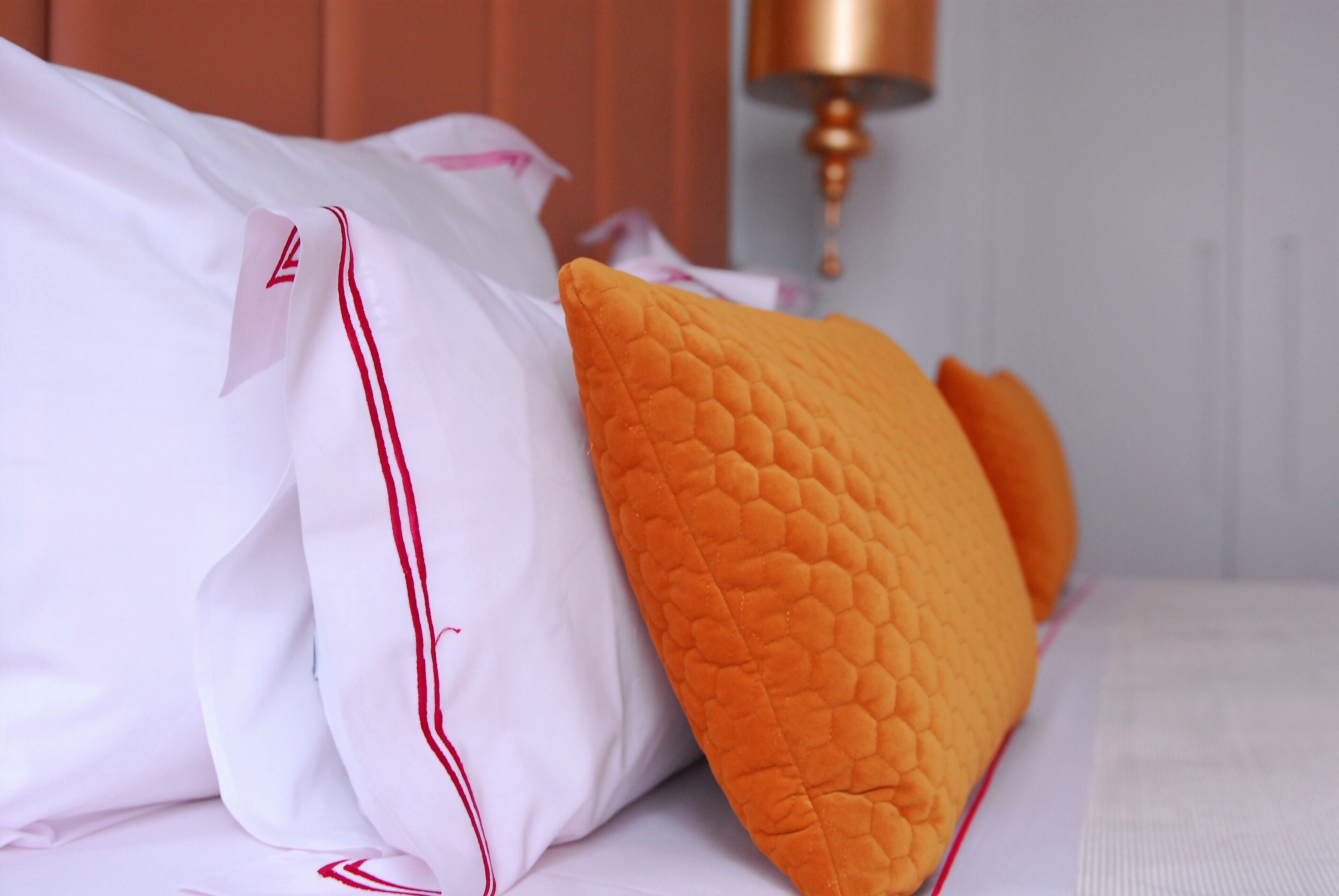 A bed with white pillows and an orange quilted pillow.