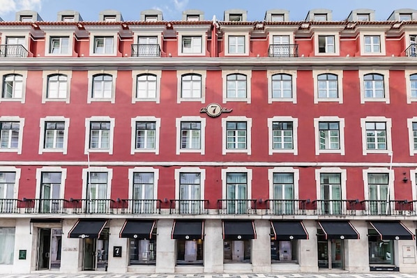 A red building with white window frames, a sign with the number 7, and black awnings over the entrance.