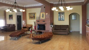 A spacious living room with a fireplace, two sofas, a coffee table, and a brown ottoman. - Athorama Hotel (Aristotelis)