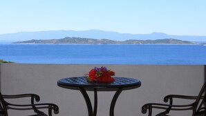 A table with a flower arrangement on a balcony overlooking a body of water and distant landforms. - Athorama Hotel (Aristotelis)