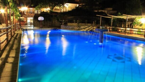 A swimming pool with a basketball hoop, surrounded by a wooden deck and a stone wall. - Athorama Hotel (Aristotelis)