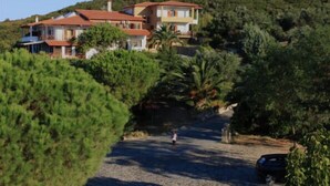 A hillside property with multiple buildings, a gravel driveway, and surrounding greenery. - Athorama Hotel (Aristotelis)