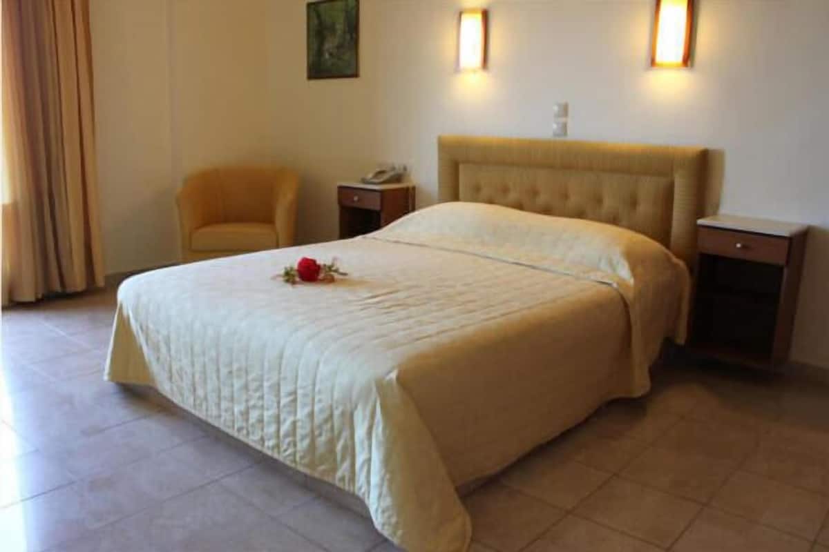 A hotel room with a large bed, a chair, bedside tables, and a wall-mounted lamp.