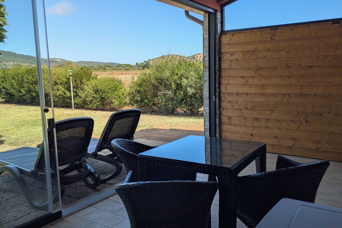 An outdoor patio with a table and chairs, a view of the countryside, and a wooden wall.