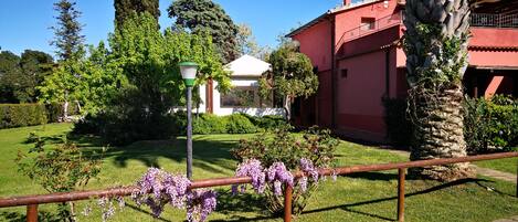 A garden with a red building, a white gazebo, and a lamp post.