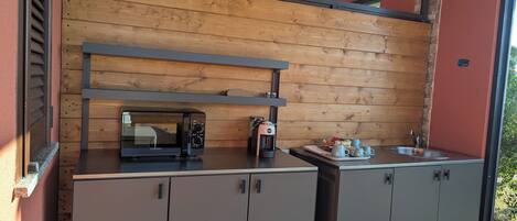 Una kitchenette compacta con microondas integrado, cafetera y una pequeña encimera con tazas y una bandeja.