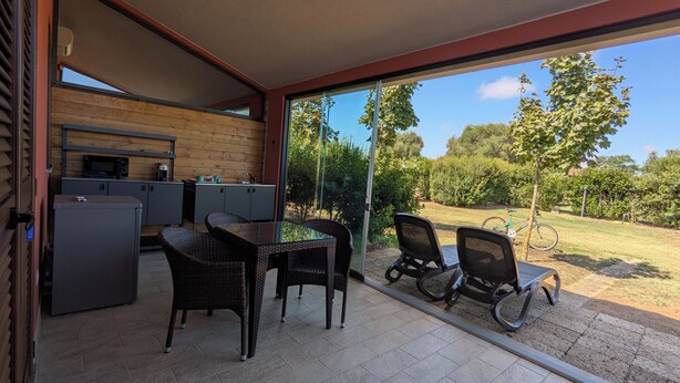 A modern outdoor kitchen area with a dining table and chairs, a bicycle, and a view of a garden. - Agrialbergo Capalbio La Sugherella (Capalbio)