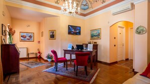A well-lit living room with a wooden floor, a red sofa, a desk with a computer, and a chandelier. - Alhambra B&B Guest House di Charme (Giarre)