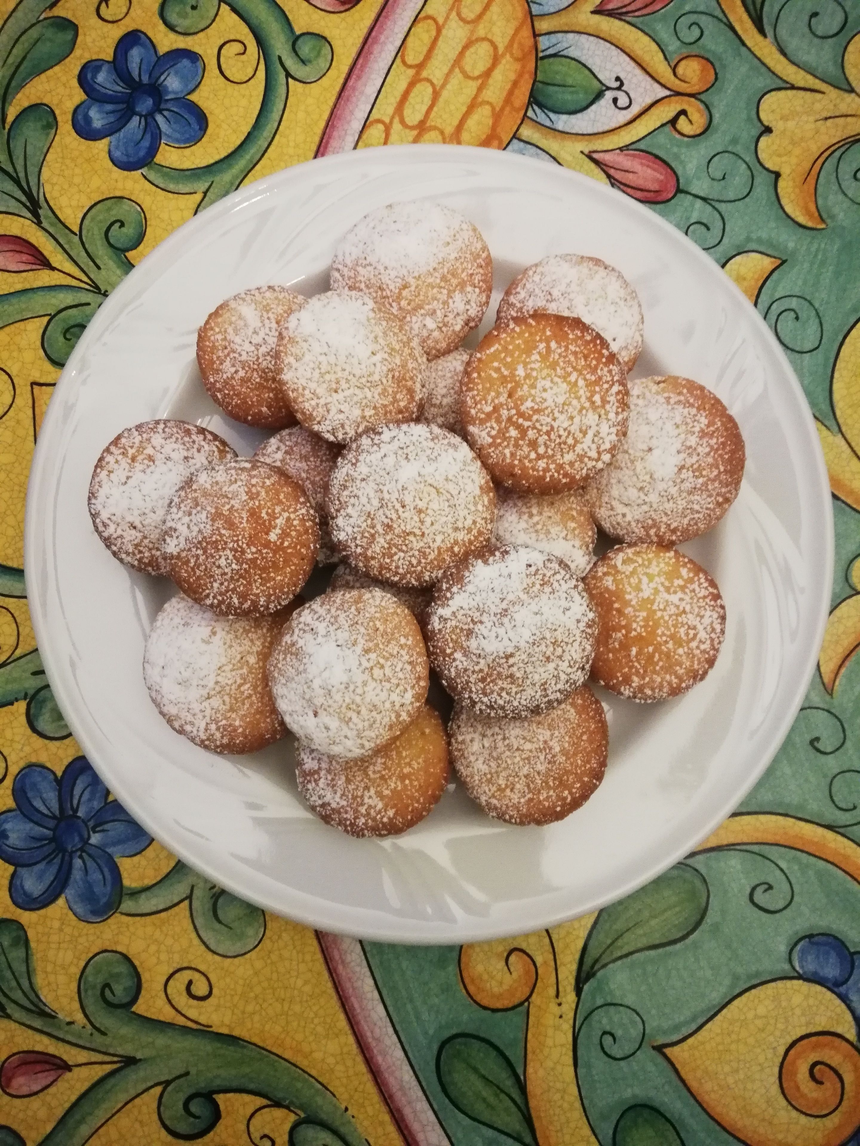 A plate of round, powdered doughnuts on a white plate.