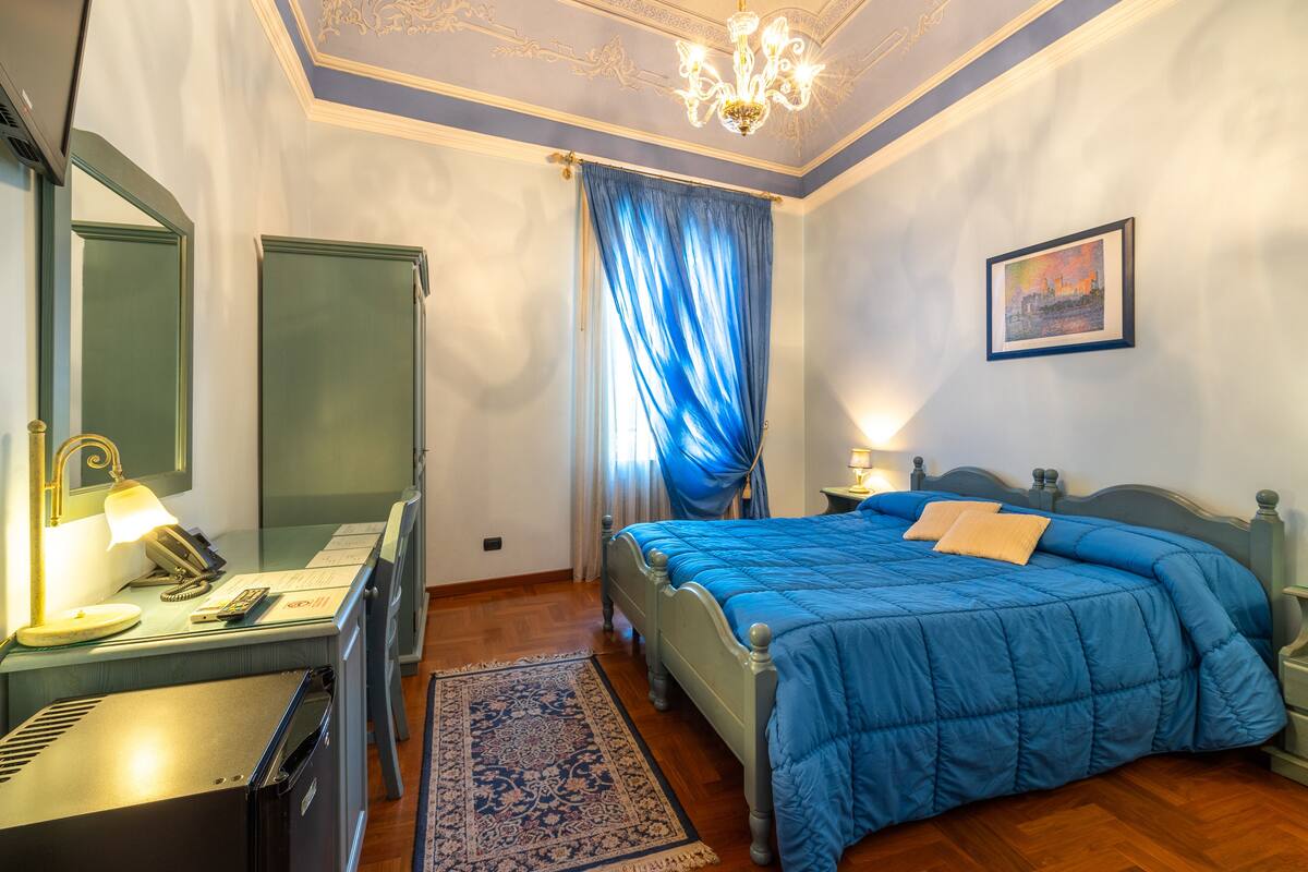 Un dormitorio con cama, escritorio, espejo, candelabro y un cuadro en la pared.