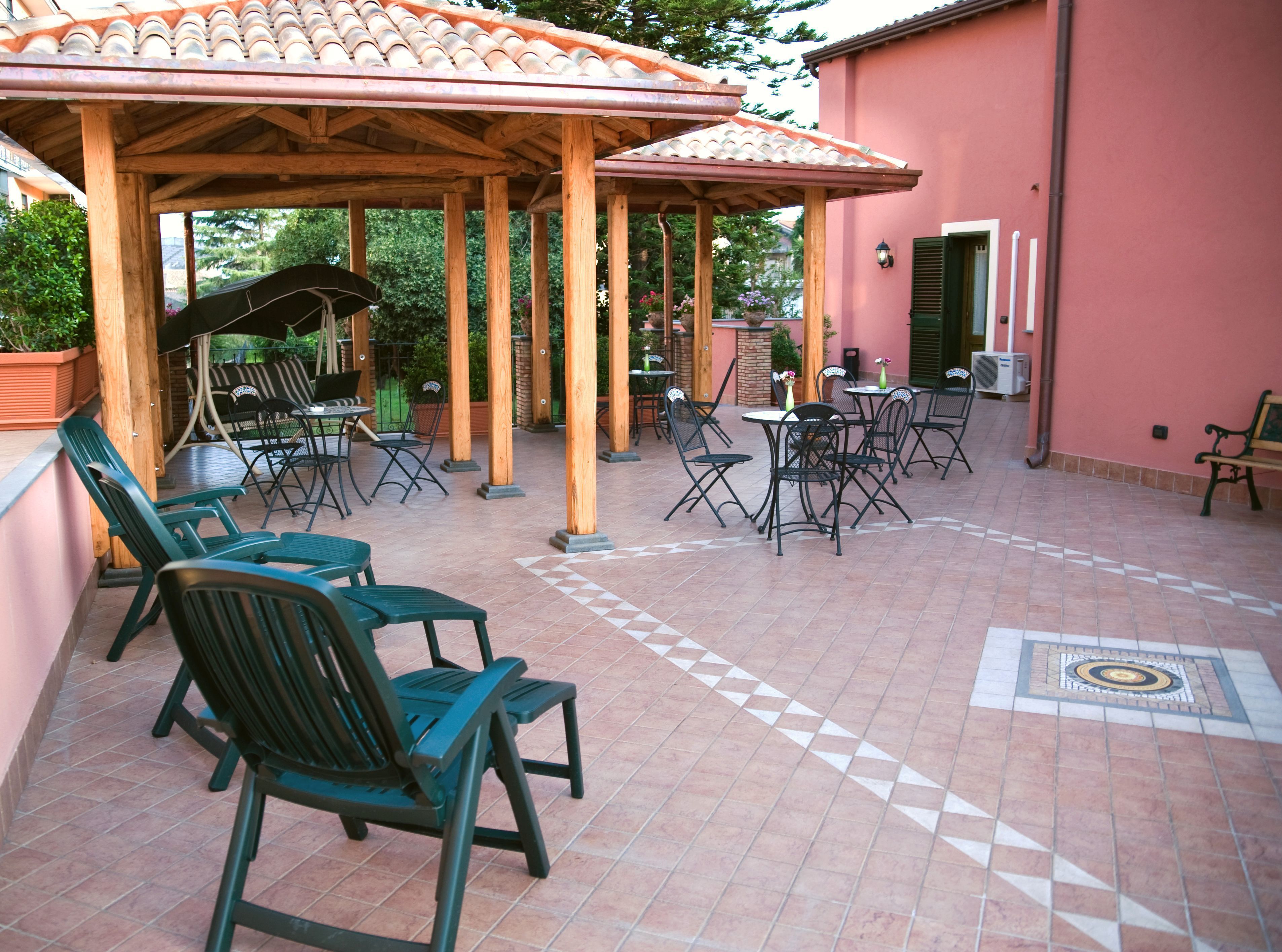 Un patio al aire libre con pérgolas de madera, sillas y mesas verdes.