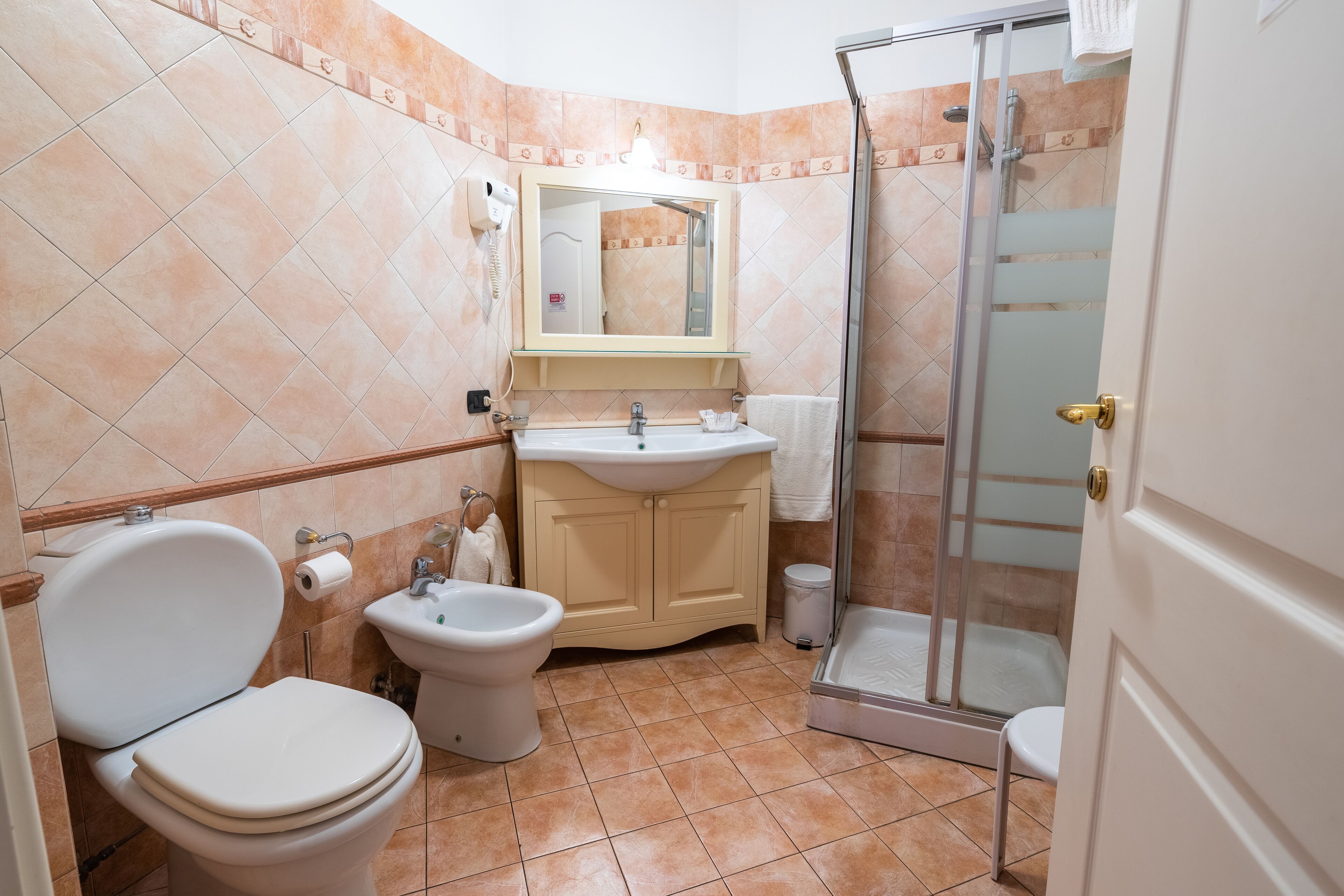 Un baño con inodoro, bidé, lavabo y ducha con mampara de vidrio.