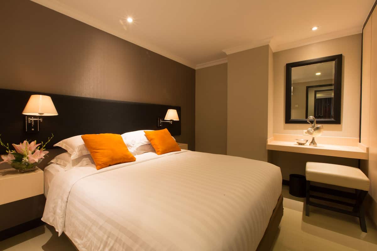 A hotel room with a large bed, two bedside lamps, a small table with a mirror, and a bench.