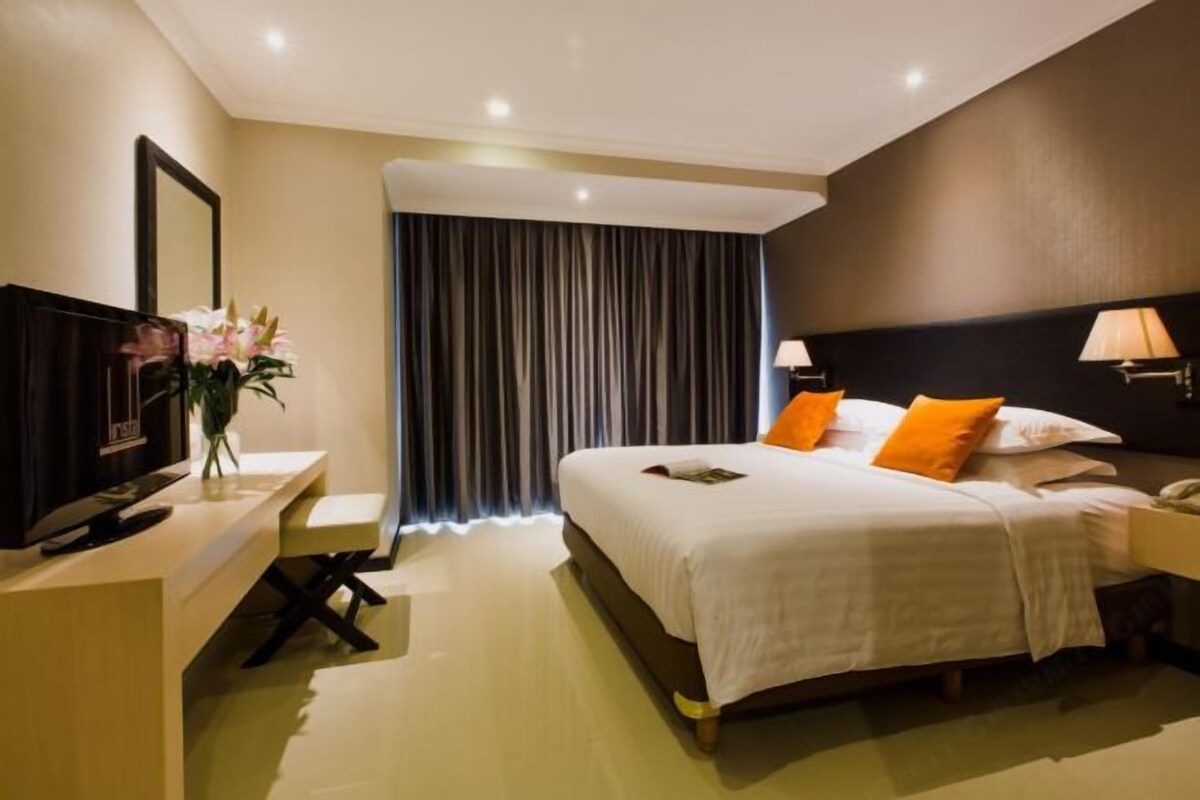 A hotel room with a bed, bedside lamps, a desk with a television, and a large window with curtains.