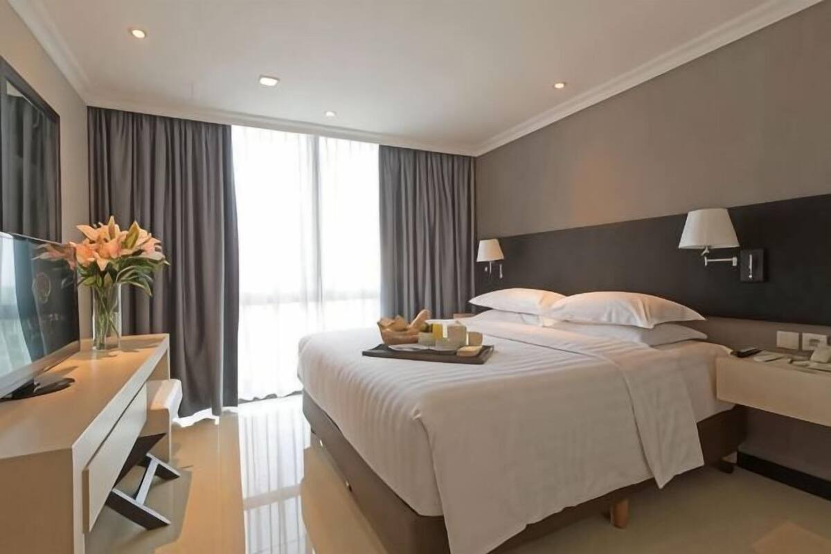 A hotel room with a bed, bedside table, lamp, and a desk with a TV.