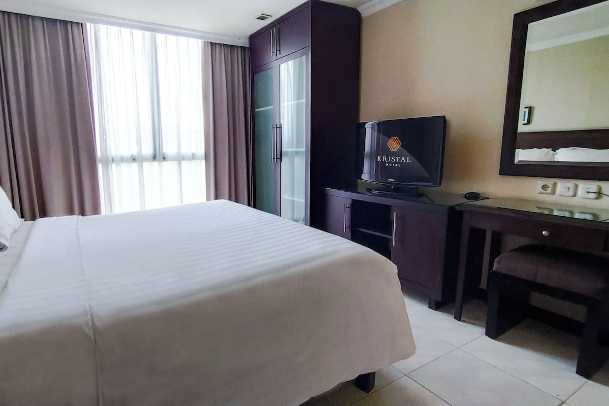 A hotel room with a large bed, a desk with a television, and a window with curtains.