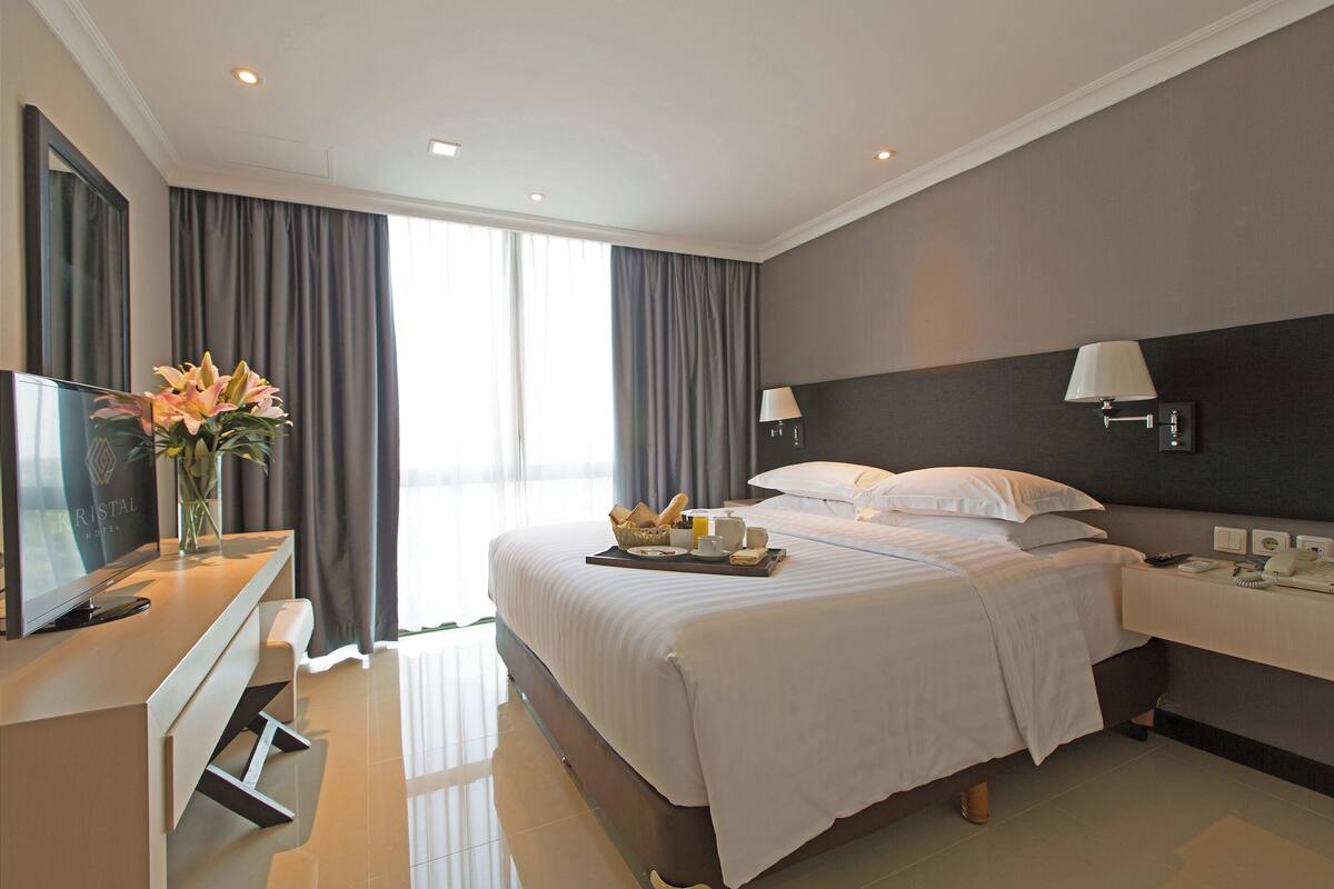 A modern hotel room with a large bed, bedside lamps, a TV, and a breakfast tray on the bed.
