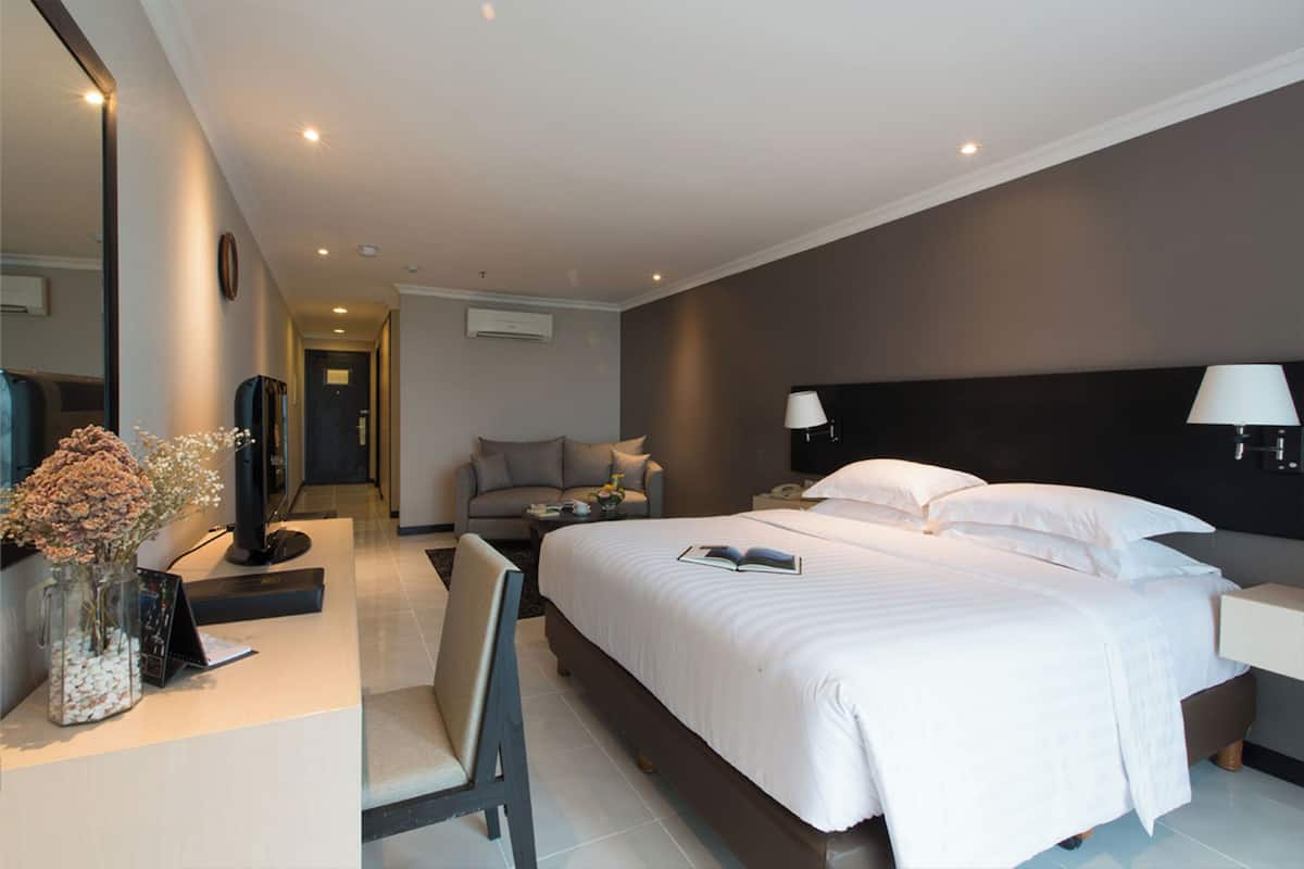 A modern hotel room with a large bed, bedside lamps, a desk with a computer, and a chair.