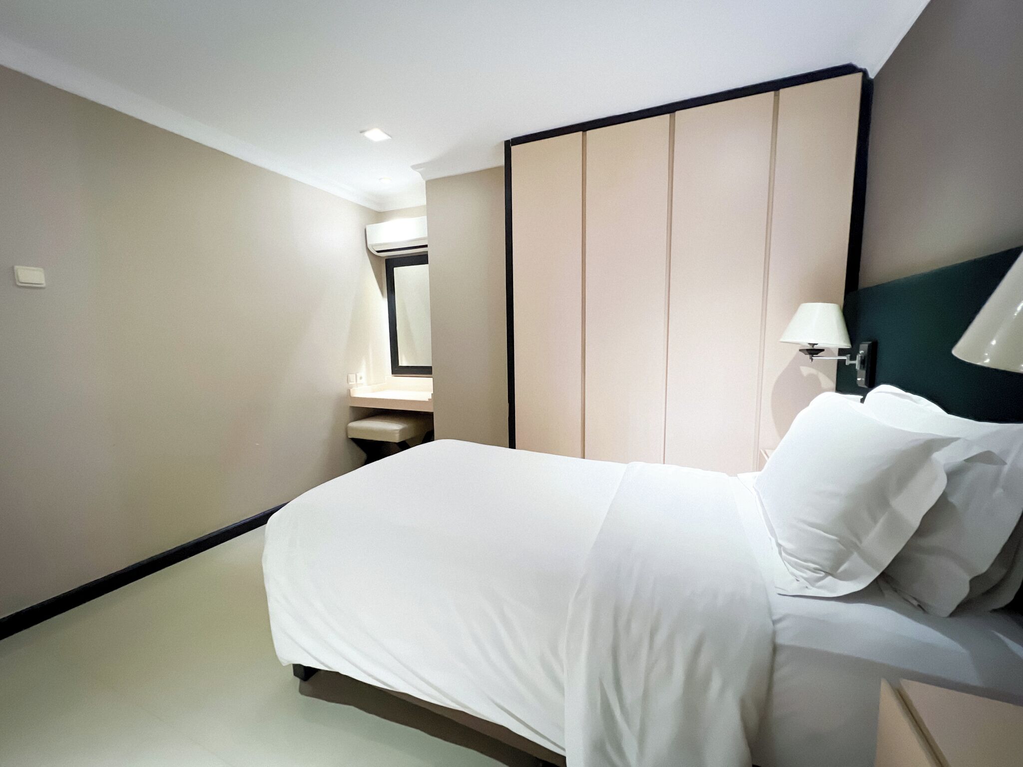 A modern hotel room with a large bed, a bedside table, a mirror, and a wall-mounted lamp.