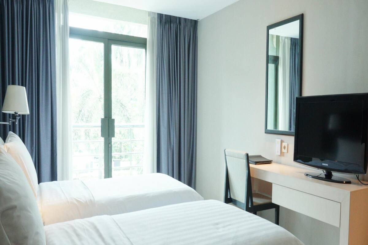 A hotel room with two beds, a desk, a television, and a window with curtains.