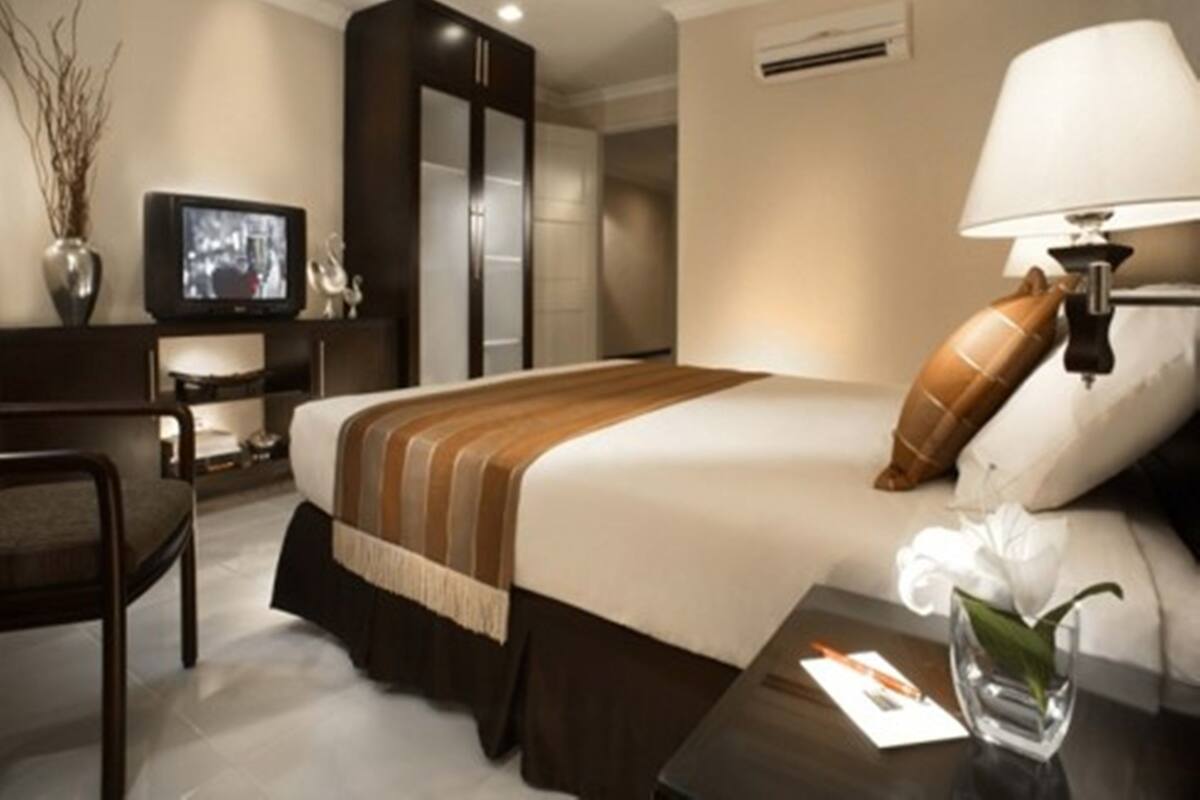 A modern hotel room with a bed, a desk with a television, a lamp, and a vase with flowers.